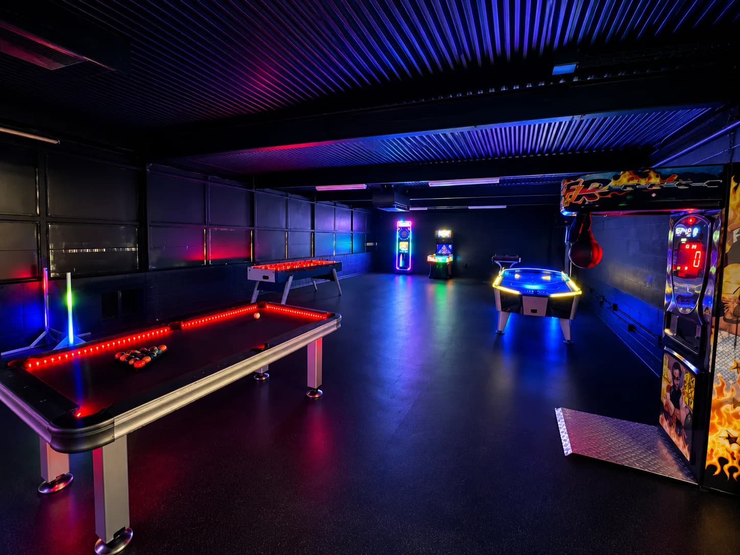 The Billiards Zone at night: an LED-lit pool table, foosball, air hockey, and arcade cabinets under neon lighting